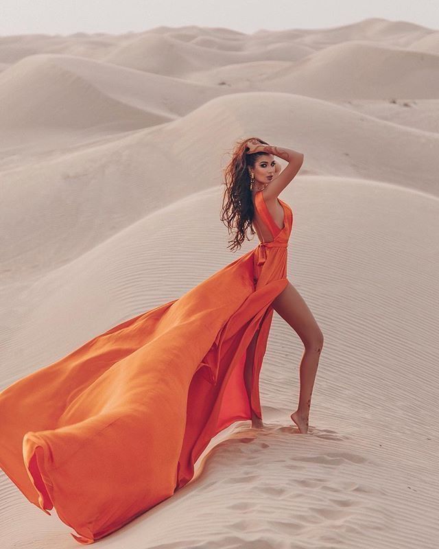 Cinematic Dubai desert fashion photoshoot with woman in flowing orange dress on sand dunes
