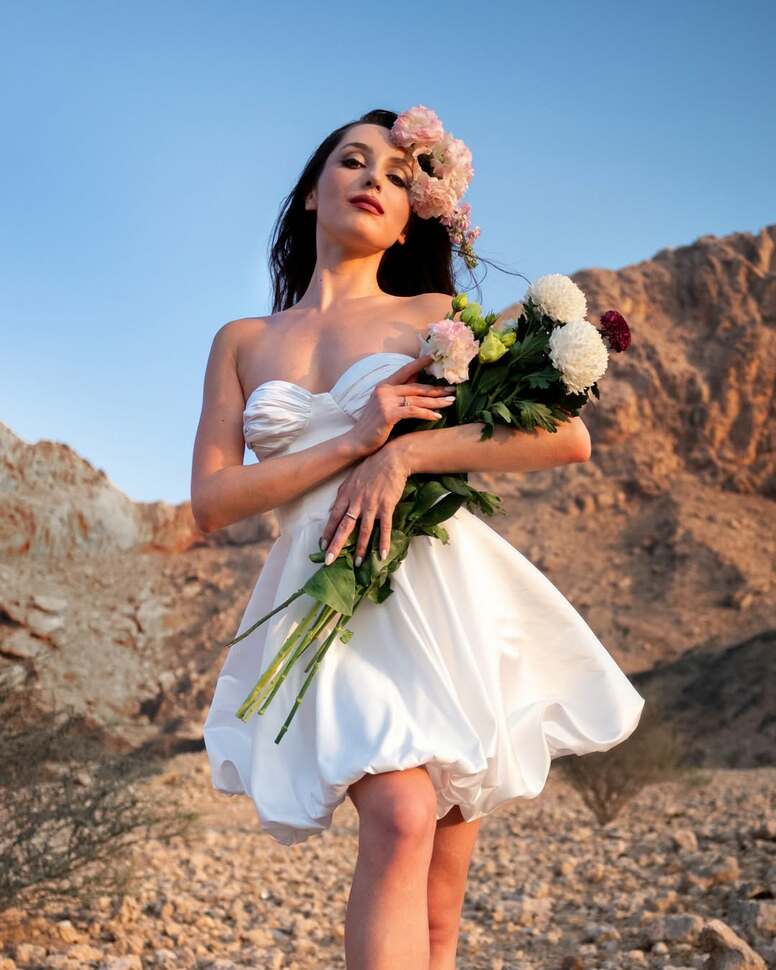 bridge in short white dress holding flowers in Dubai desert