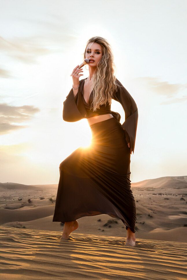 Fashion portrait of woman lying on Dubai desert sand dunes during golden hour sunset