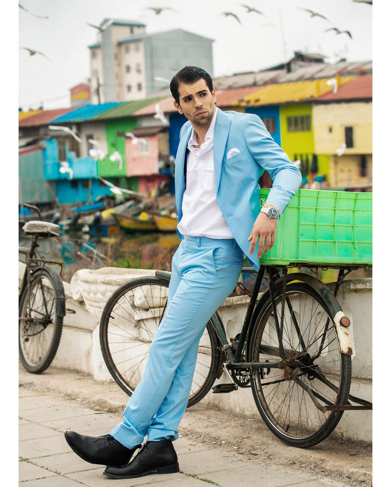 Man in a suit leading on a bicycle with colorful old house in the background
