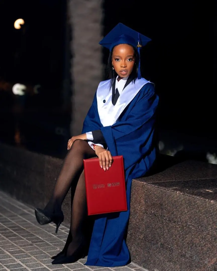 Graduate in a blue cap and gown holding a diploma folder during an outdoor graduation photoshoot at night in Dubai.